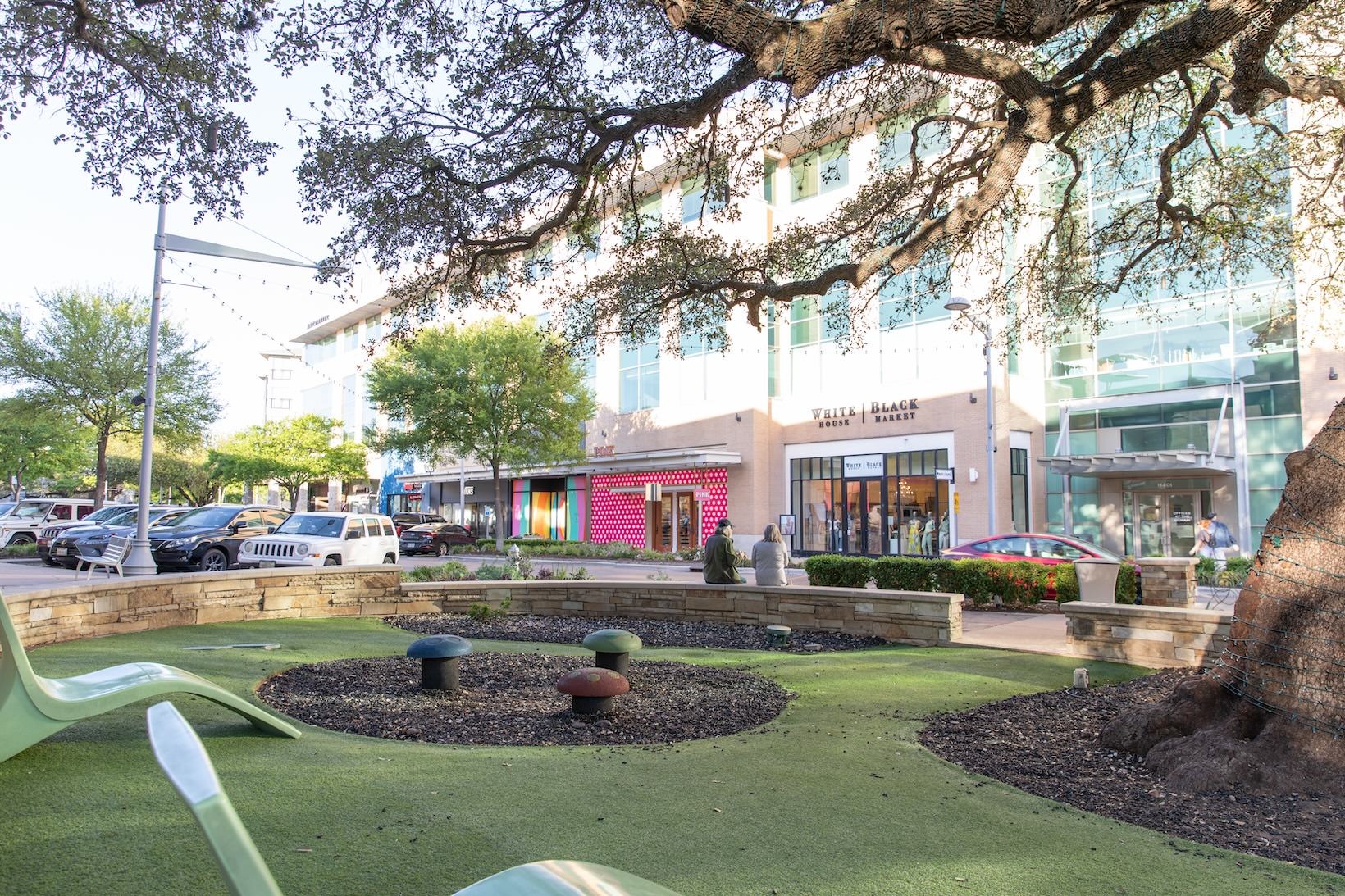 The Domain a seating area next to shops with a tree and lounge chairs