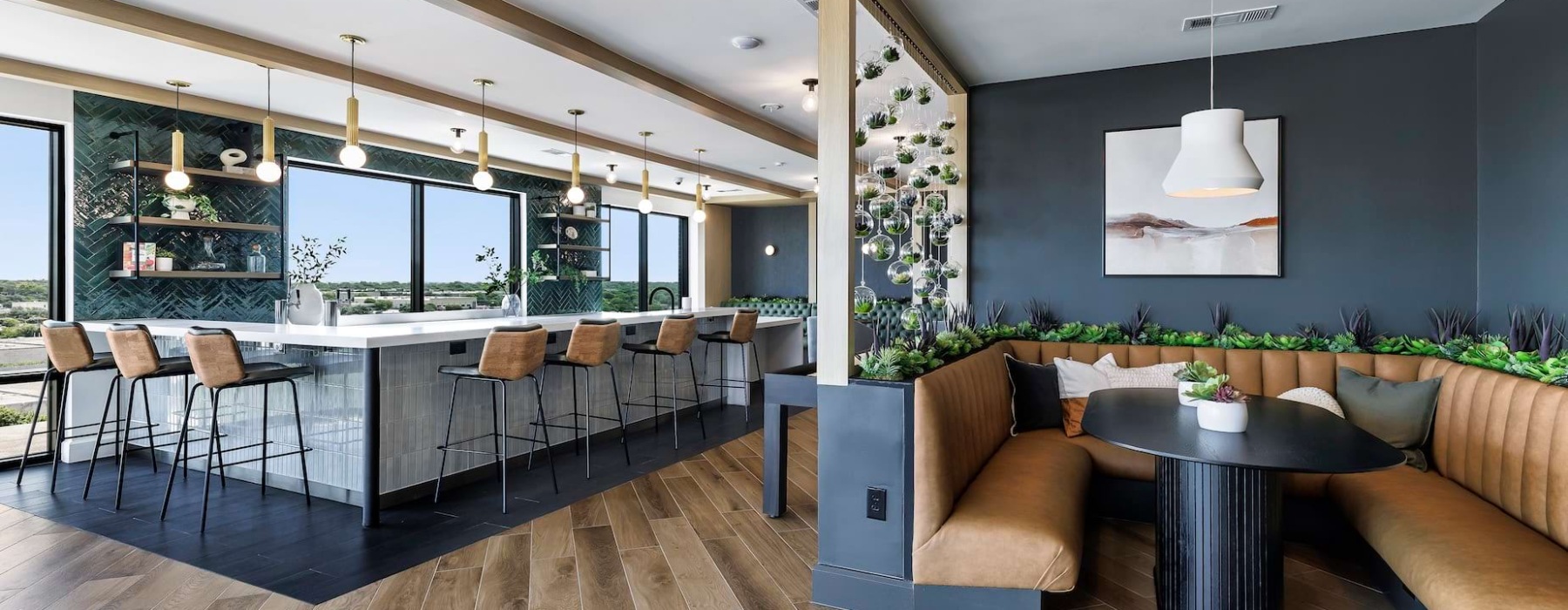 The Skylounge at The Met apartments in North Austin, TX, featuring an indoor bar and social space with a long countertop and bar seating, a large booth and table, and ample lighting and greenery.