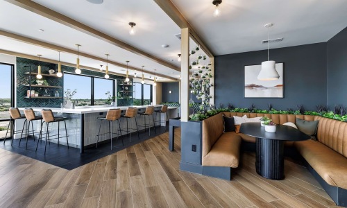 The Skylounge at The Met apartments in North Austin, TX, featuring an indoor bar and social space with a long countertop and bar seating, a large booth and table, and ample lighting and greenery.