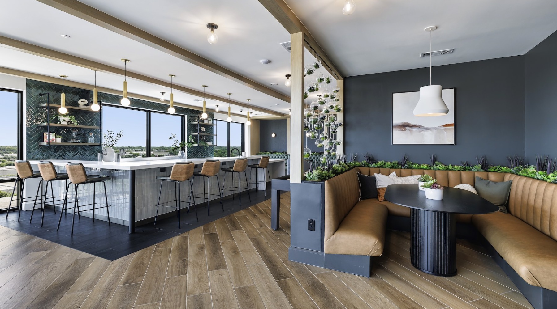 The Skylounge at The Met apartments in North Austin, TX, featuring an indoor bar and social space with a long countertop and bar seating, a large booth and table, and ample lighting and greenery.