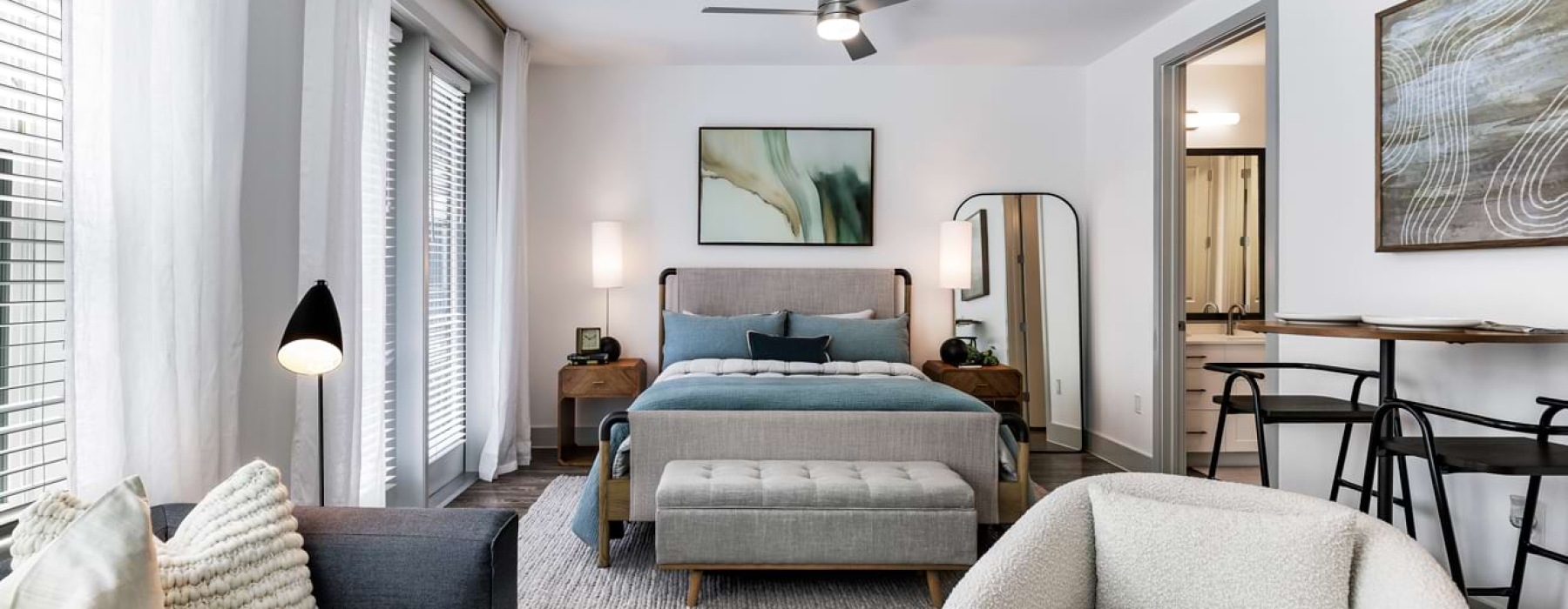 A view of a bed, sofa, and dining space with large windows and ample lighting at The Met apartments. 
